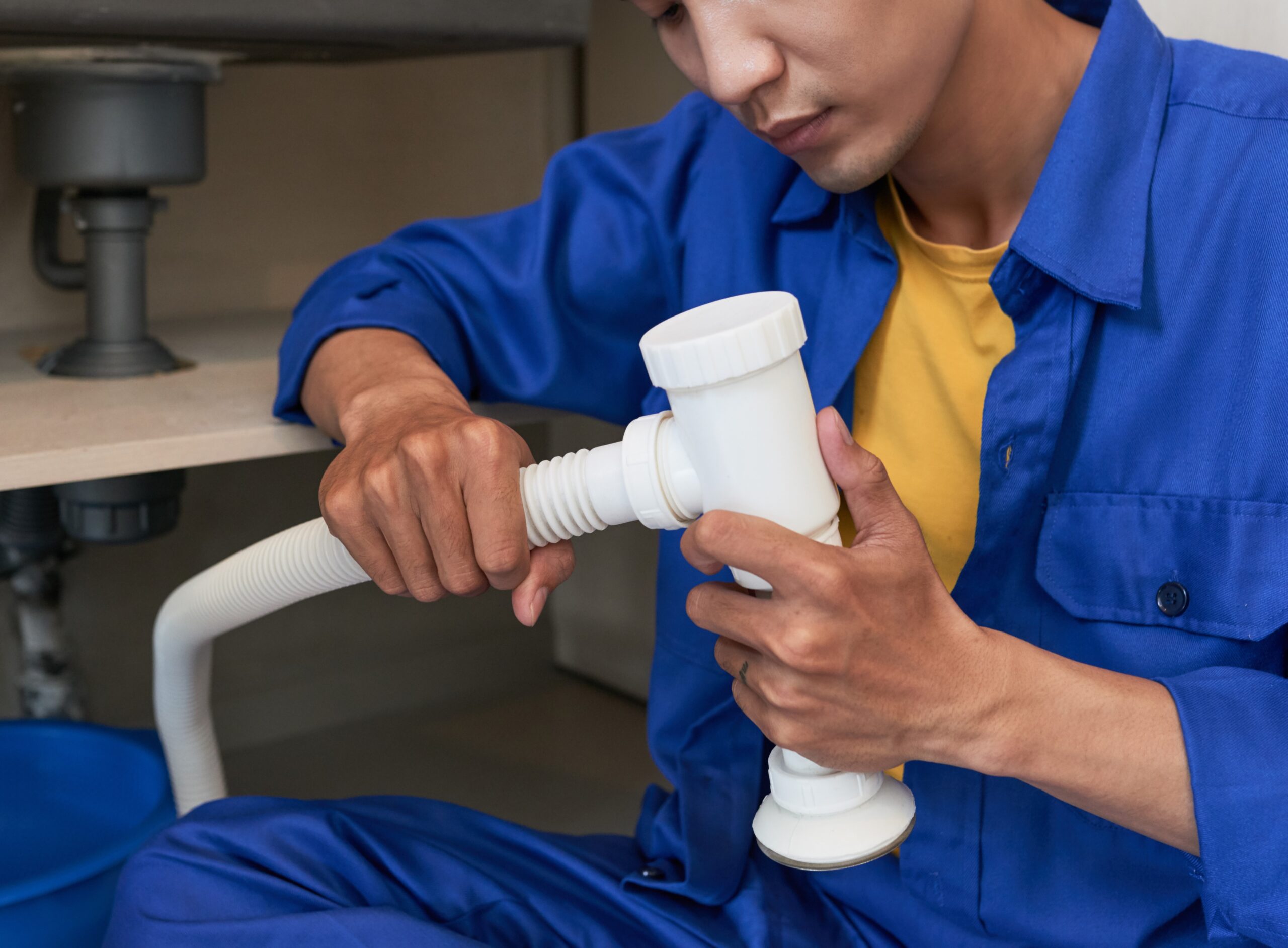 Young professional plumber concentrated on assembling sink pipe